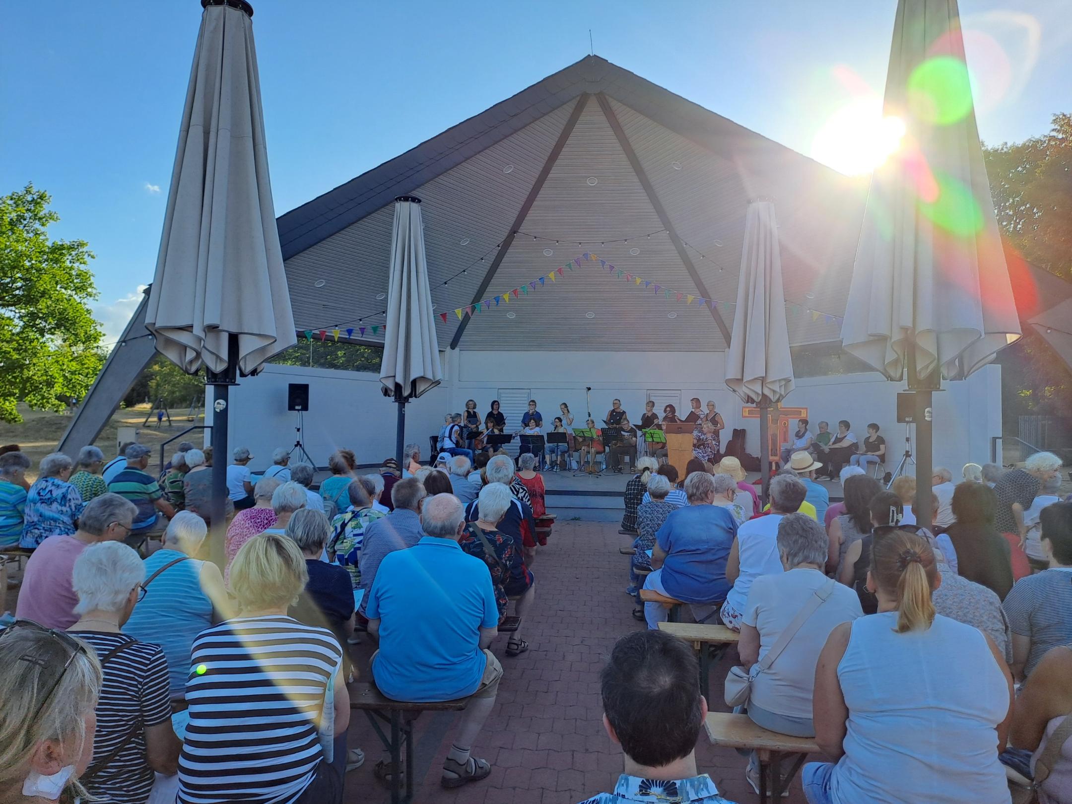 Man sieht  wie Besucher des Abendlobs mit dem mit dem Gesicht nach vorne zum Musikpavillon gerichtet am Abendlob 2026 teilnehmen. Im Hintergrund ist der Musikpavillon zu sehen.