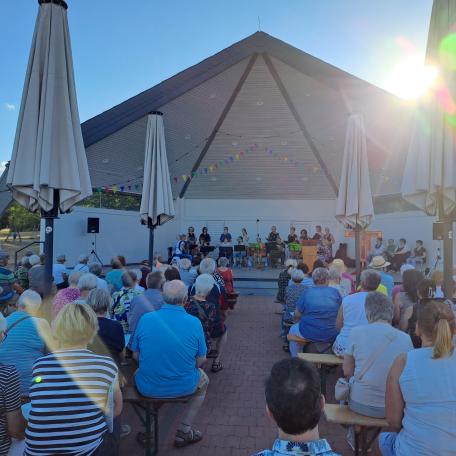 Man sieht  wie Besucher des Abendlobs mit dem mit dem Gesicht nach vorne zum Musikpavillon gerichtet am Abendlob 2026 teilnehmen. Im Hintergrund ist der Musikpavillon zu sehen.