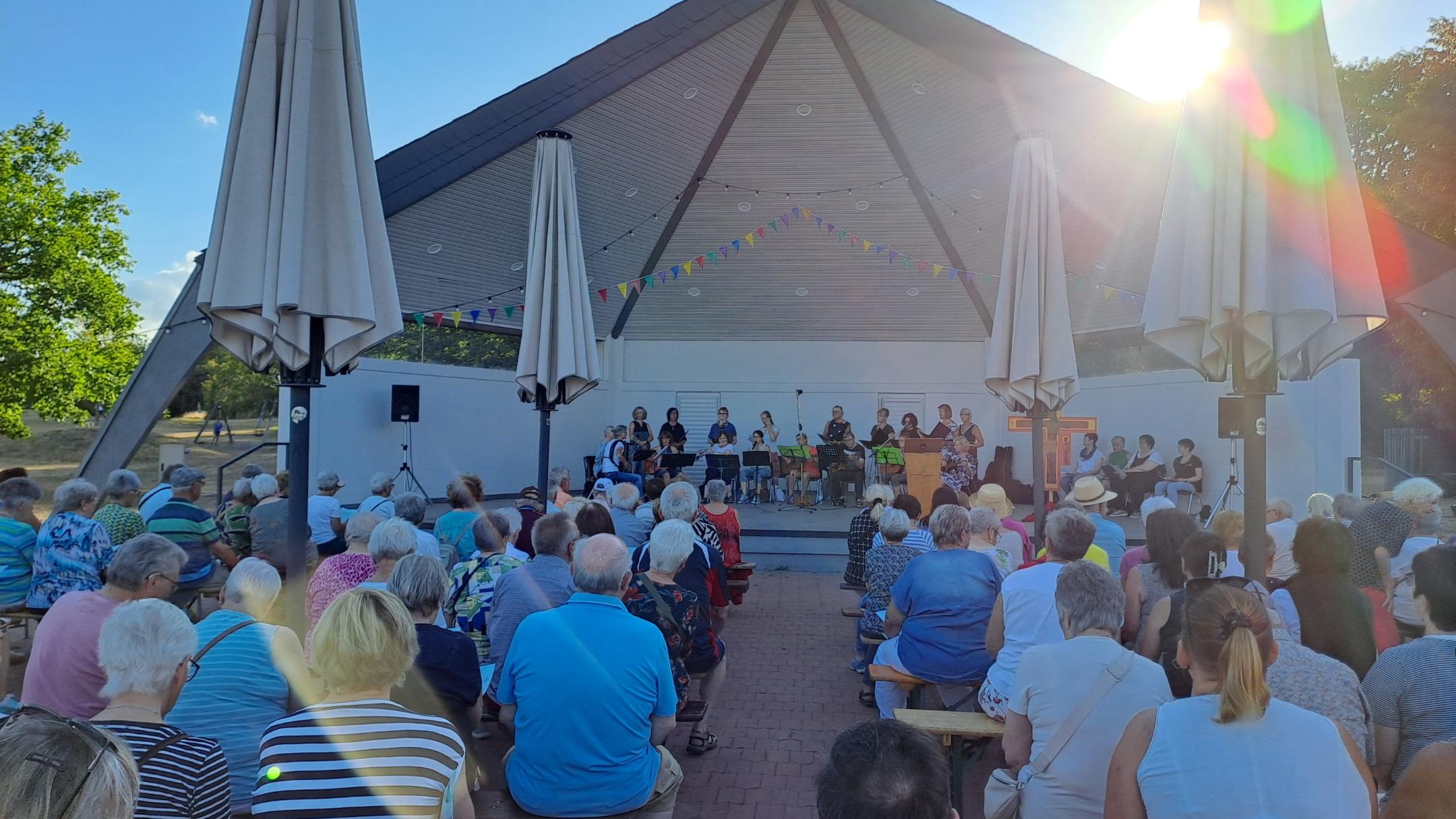 Man sieht wie Besucher des Abendlobs mit dem mit dem Gesicht nach vorne zum Musikpavillon gerichtet am Abendlob 2026 teilnehmen. Im Hintergrund ist der Musikpavillon zu sehen.