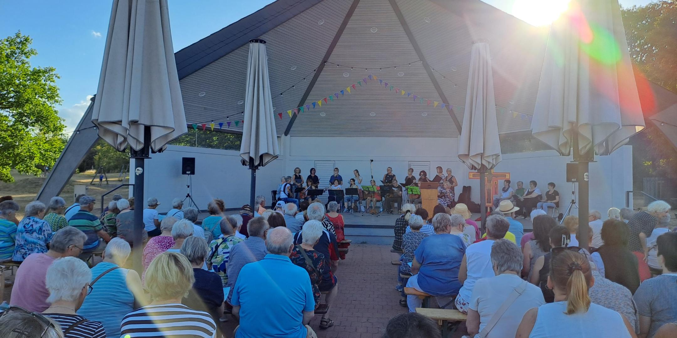 Man sieht wie Besucher des Abendlobs mit dem mit dem Gesicht nach vorne zum Musikpavillon gerichtet am Abendlob 2026 teilnehmen. Im Hintergrund ist der Musikpavillon zu sehen.