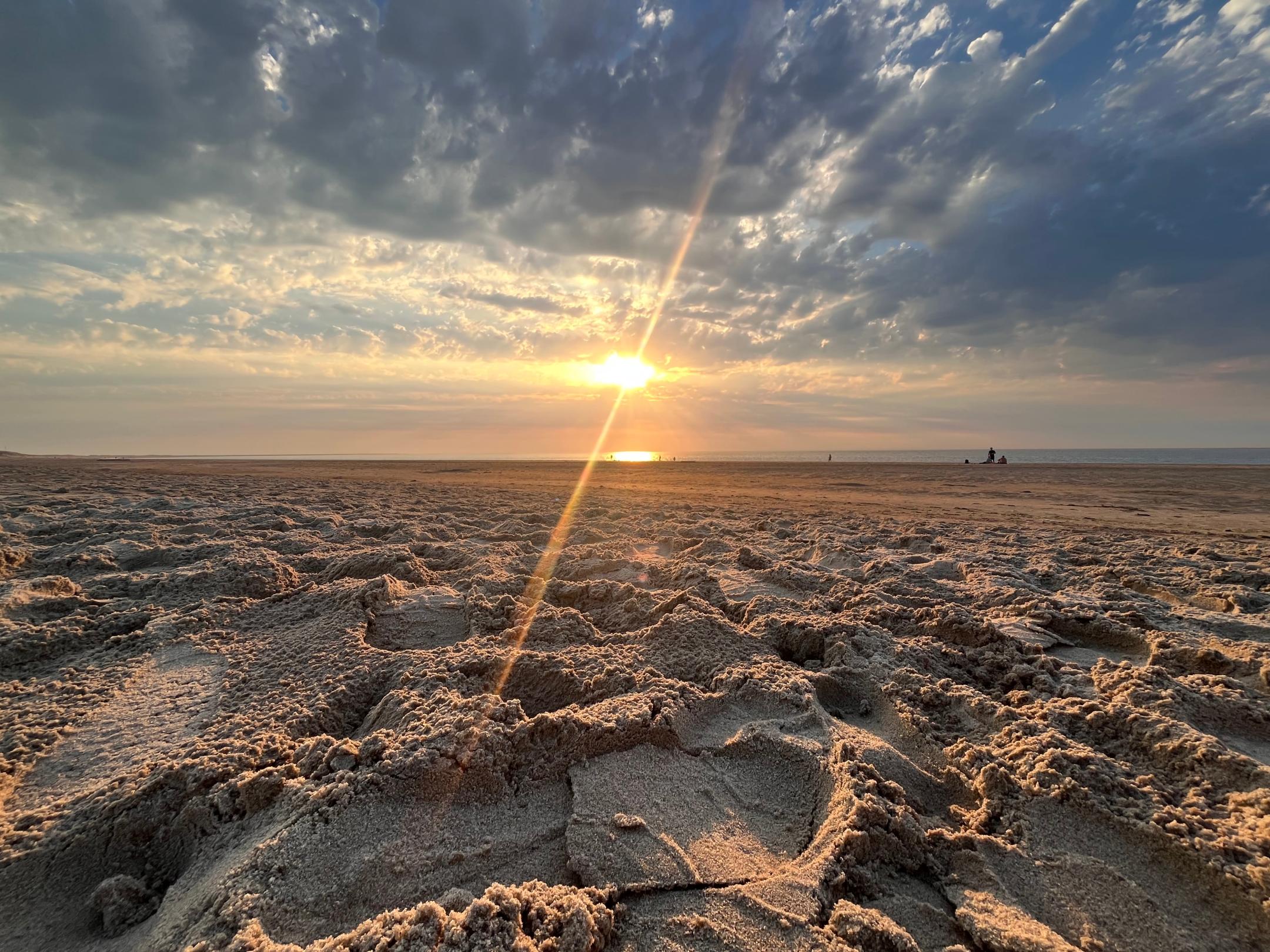 Im Vordergrund sieht man einen Sandstrand und am Horizont die aufgehende Sonne