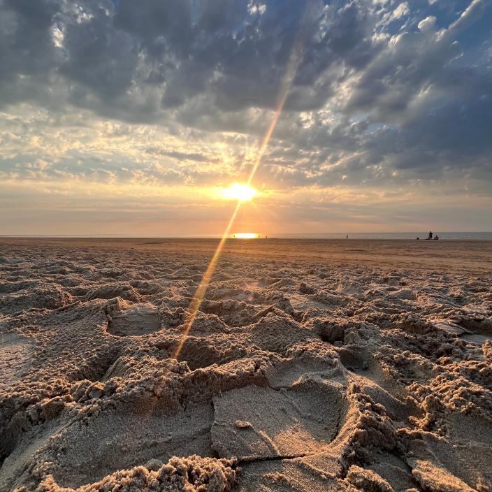 Im Vordergrund sieht man einen Sandstrand und am Horizont die aufgehende Sonne