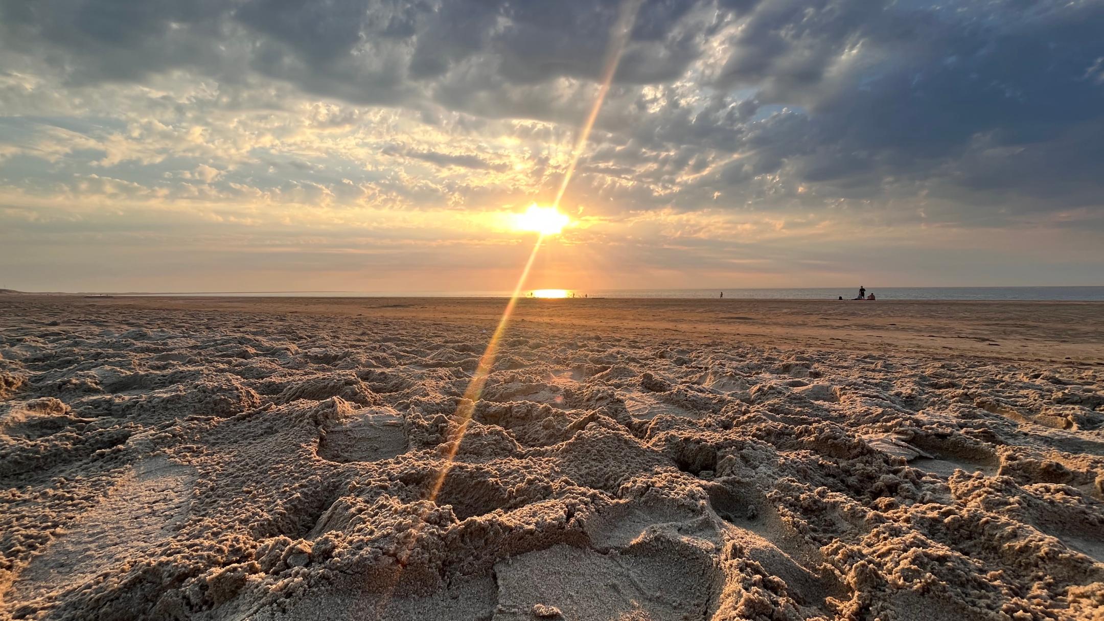 Im Vordergrund sieht man einen Sandstrand und am Horizont die aufgehende Sonne