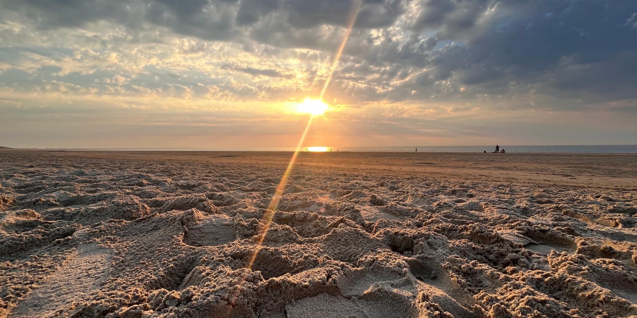 Im Vordergrund sieht man einen Sandstrand und am Horizont die aufgehende Sonne